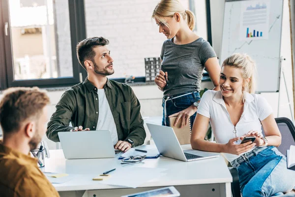 Grupo de jóvenes empresarios que trabajan con ordenadores portátiles y charlan juntos en la oficina - foto de stock