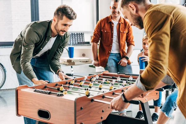 Grupo de jóvenes empresarios casuales jugando al futbolín en la oficina y divirtiéndose juntos - foto de stock