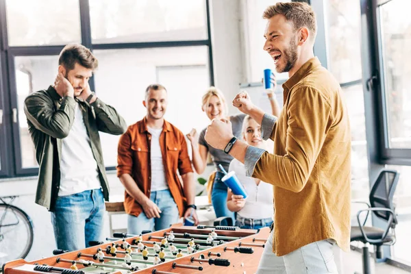 Expressivo pessoas de negócios casuais jogando futebol de mesa no escritório e se divertindo juntos — Fotografia de Stock