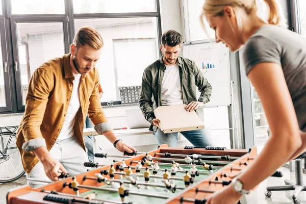 Gruppo di felici uomini d'affari casual che giocano a calcio balilla in ufficio e si divertono insieme — Foto stock