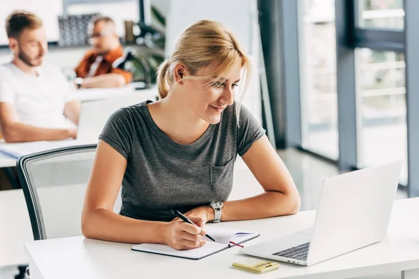 Glückliche junge Frau arbeitet mit Laptop im Großraumbüro — Stockfoto