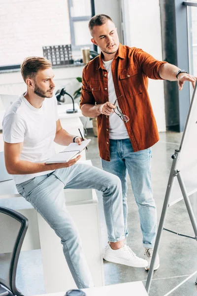 Handsome young businessmen pointing at whiteboard at office — Stock Photo