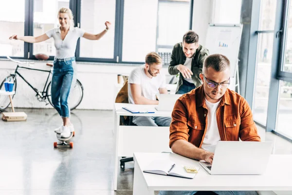 Grupo de jovens empreendedores progressistas que trabalham na startup juntos no escritório moderno espaço aberto, enquanto mulher andar de skate em segundo plano — Fotografia de Stock