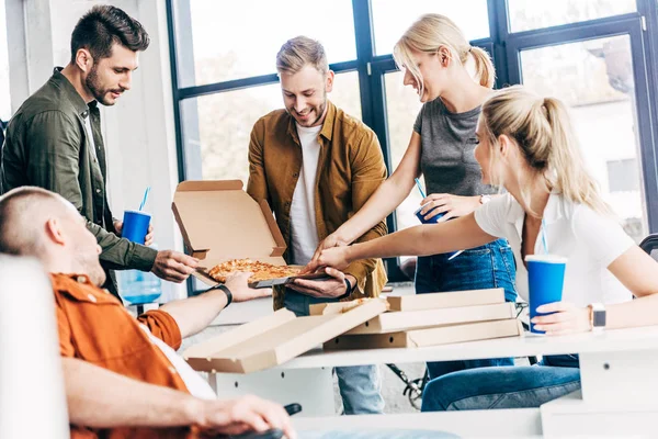 Empresarios felices exitosos comiendo pizza juntos mientras trabajan en la puesta en marcha en la oficina - foto de stock