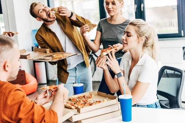 Gruppo di giovani imprenditori che mangiano pizza a pranzo insieme mentre lavorano alla startup in ufficio — Foto stock