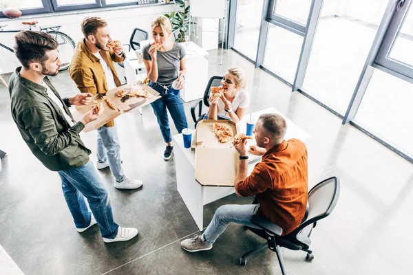 Vue grand angle du groupe de jeunes entrepreneurs ayant pizza pour le déjeuner ensemble tout en travaillant sur le démarrage au bureau — Photo de stock