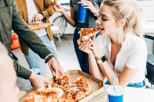 Schnappschuss einer Frau, die mit Kollegen beim Mittagessen Pizza isst, während sie im Büro am Start-up arbeitet — Stockfoto