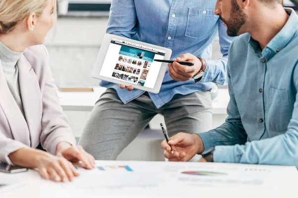 Cropped shot of businessman showing digital tablet with amazon website to colleagues at workplace — Stock Photo