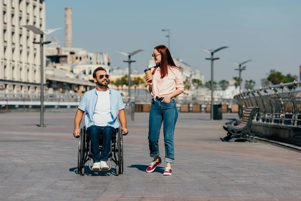 Bonito namorado em cadeira de rodas e namorada com copo de café descartável ter andar na rua — Stock Photo