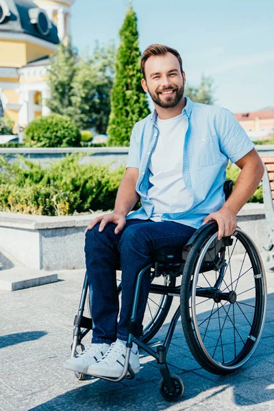 Smiling handsome man in wheelchair looking at camera on street — Stock Photo