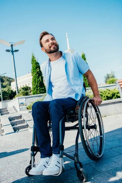 Hombre guapo en silla de ruedas mirando hacia arriba en la calle — Stock Photo