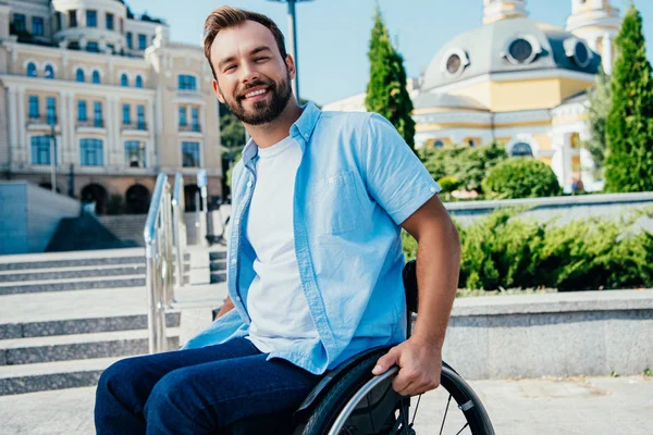 Cheerful handsome man in wheelchair looking at camera on street — Stock Photo