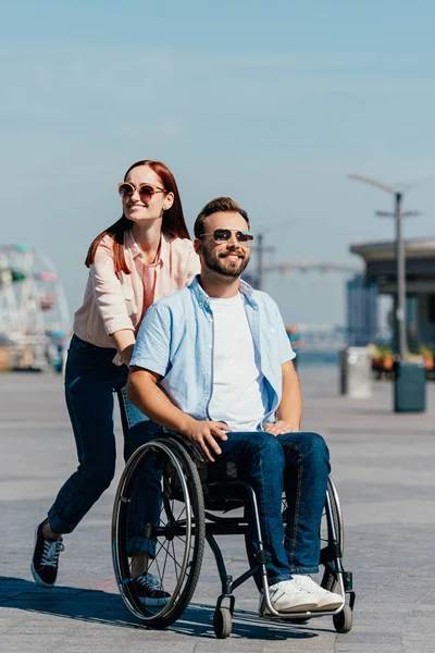 Atraente namorada empurrando bonito namorado deficiente em cadeira de rodas na rua — Fotografia de Stock