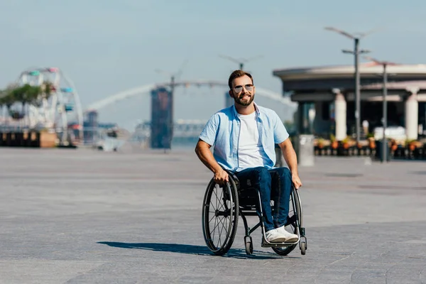 Joyeux bel homme en lunettes de soleil en fauteuil roulant dans la rue — Photo de stock