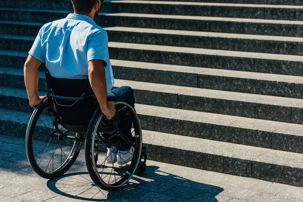 Visão traseira do homem com deficiência usando cadeira de rodas na rua e parando perto de escadas sem rampa — Fotografia de Stock