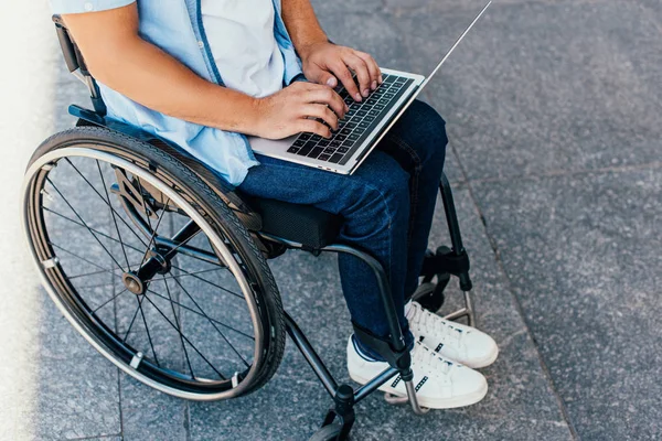 Imagen recortada del hombre en silla de ruedas utilizando el ordenador portátil en la calle - foto de stock