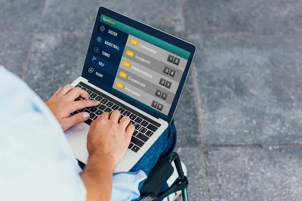 Cropped image of man in wheelchair using laptop with sportbets appliance on street — Stock Photo