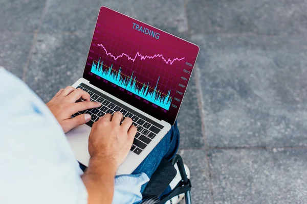 Cropped image of man in wheelchair using laptop with traiding appliance on street — Stock Photo