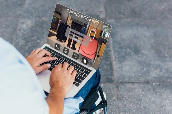 Imagen recortada del hombre en silla de ruedas utilizando el ordenador portátil con sitio web de reserva en línea en la calle - foto de stock