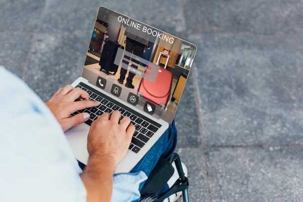 Cropped image of man in wheelchair using laptop with online booking website on street — Stock Photo