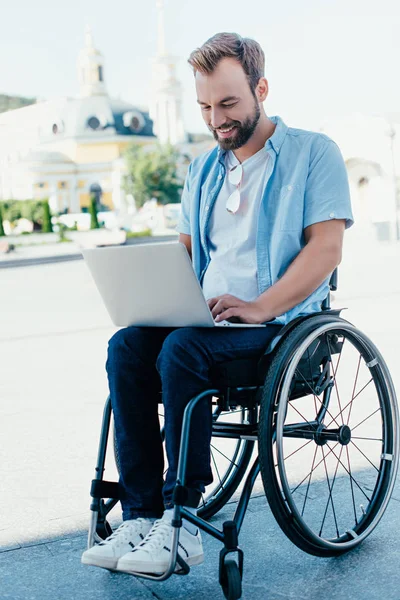 Homem bonito em cadeira de rodas usando laptop na rua — Fotografia de Stock