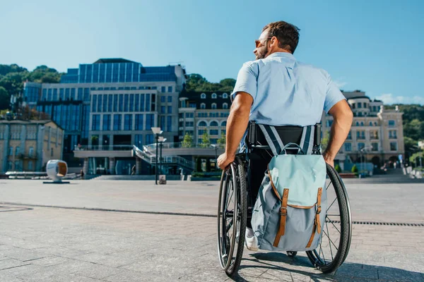 Vue arrière de l'homme en fauteuil roulant avec sac sur la rue — Photo de stock