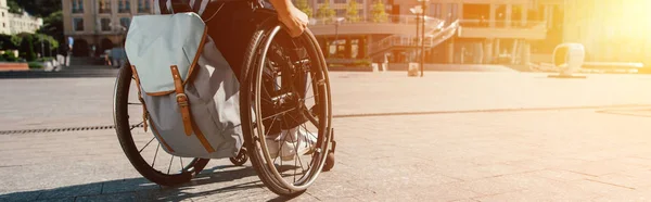 Cropped panoramic view of man using wheelchair with bag on street with sunlight — Stock Photo