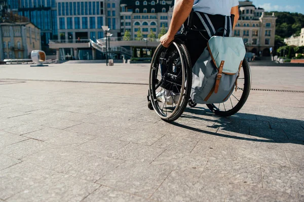 Imagen recortada de hombre usando silla de ruedas con bolsa en la ciudad - foto de stock