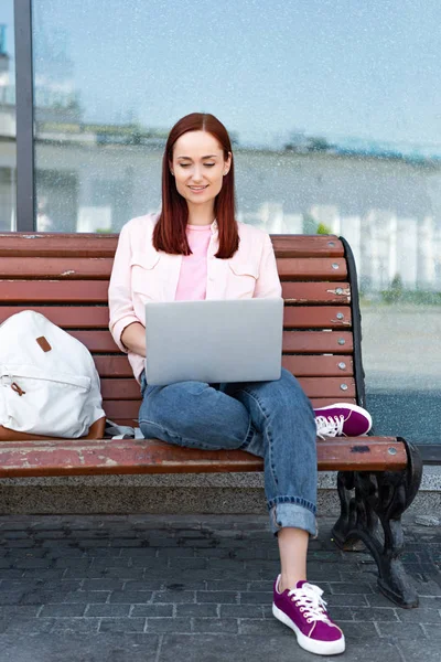 Attractive freelancer using laptop on bench in city — Stock Photo