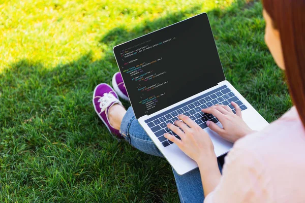 Обітнутого зображення жінки, використовуючи ноутбук з html-код в парку — Stock Photo