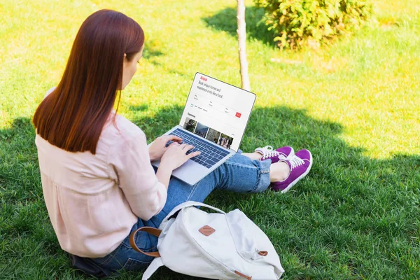 Femme attrayante en utilisant un ordinateur portable avec la page airbnb chargée dans le parc — Photo de stock