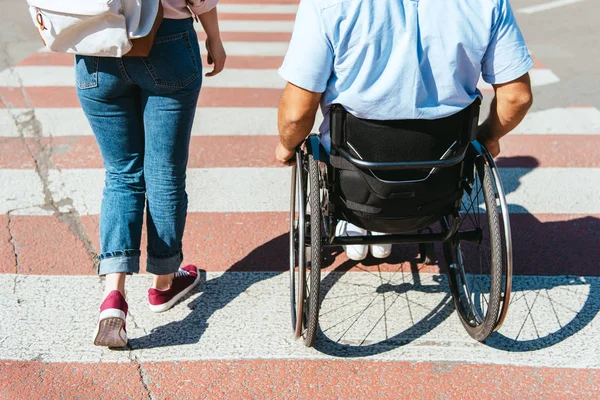 Cropped image of boyfriend in wheelchair and girlfriend crossing crosswalk in city — Stock Photo