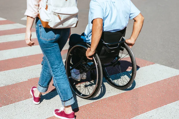 Cropped image of disabled boyfriend in wheelchair and girlfriend crossing crosswalk in city — Stock Photo