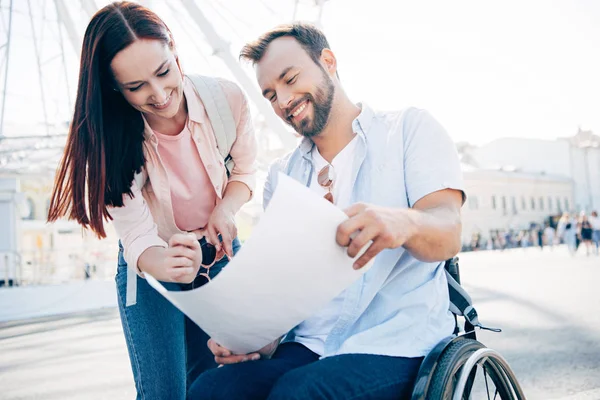 Sourire beau petit ami en fauteuil roulant et petite amie regardant la carte sur la rue — Photo de stock