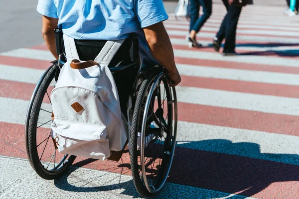 Cropped image of man in wheelchair with bag riding on crosswalk — Stock Photo