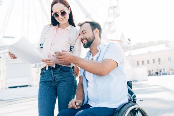 Smiling travelers using smartphone and map on street — Stock Photo