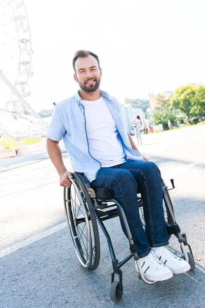 Uomo bello sorridente che utilizza sedia a rotelle sulla strada e guardando la fotocamera — Foto stock