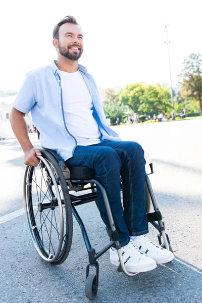 Handsome smiling man using wheelchair on street and looking up — Stock Photo