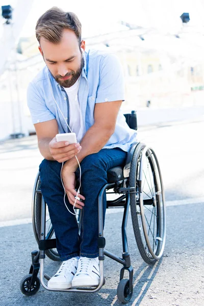 Schöner Mann im Rollstuhl hört Musik und benutzt Smartphone auf der Straße — Stockfoto