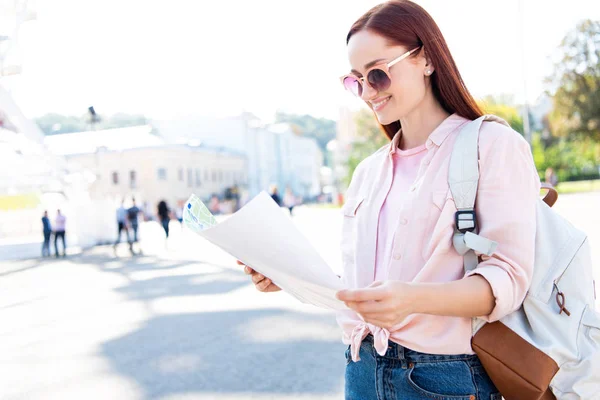 Sourire attrayant touriste dans les lunettes de soleil en regardant la carte sur la rue — Photo de stock