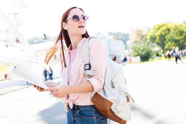 Überraschte attraktive Touristin mit Sonnenbrille, die mit Karte auf der Straße steht und nach oben schaut — Stockfoto