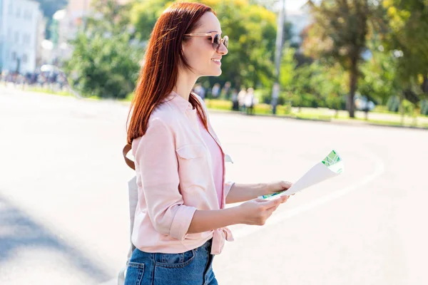 Side view of attractive smiling traveler in sunglasses standing with map on street — Stock Photo