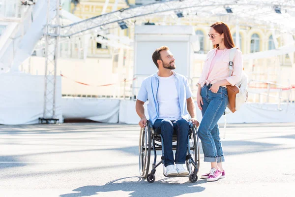 Handsome boyfriend in wheelchair and girlfriend looking at each other on street — Stock Photo