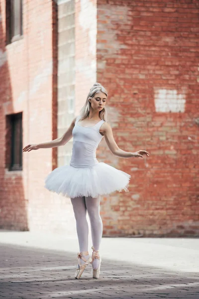 Vue pleine longueur de la jeune ballerine attrayante en tutu blanc et chaussures pointe dansant sur la rue — Photo de stock