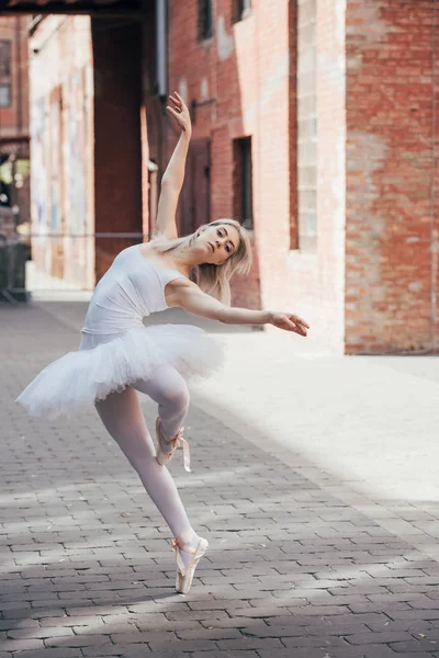 Beautiful elegant young ballerina looking at camera while dancing on city street — Stock Photo
