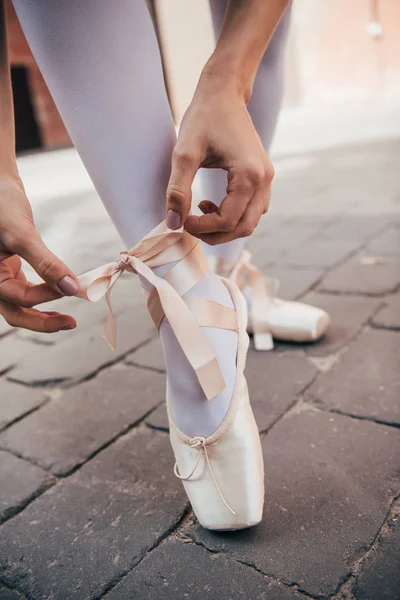 Close-up partial view of young ballerina tying pointe shoe on street — Stock Photo