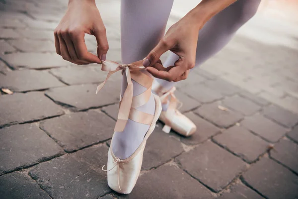 Cropped shot of young ballerina tying pointe shoe on street — Stock Photo