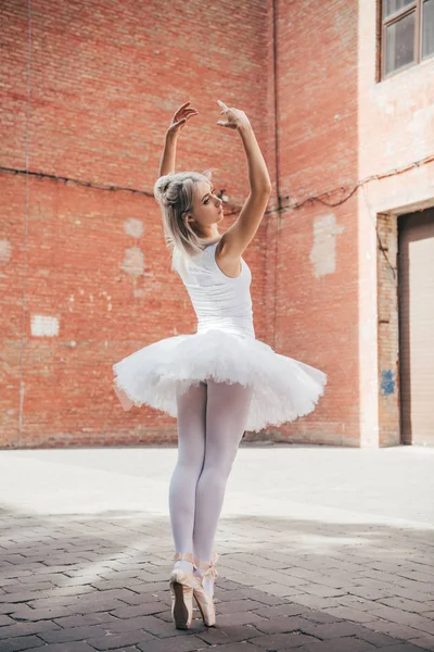 Back view of young ballerina in tutu and ballet shoes dancing on street — Stock Photo