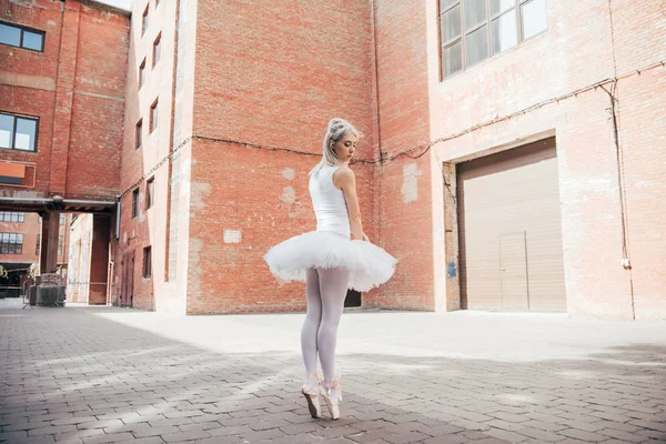 Vista completa de la joven bailarina en tutú blanco y zapatos puntiagudos bailando en la calle - foto de stock