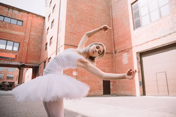 Low angle view of young ballerina in white tutu dancing on street — Stock Photo